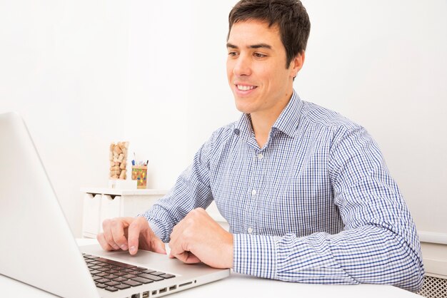 Retrato de un hombre de negocios joven sonriente que usa el ordenador portátil en la tabla blanca