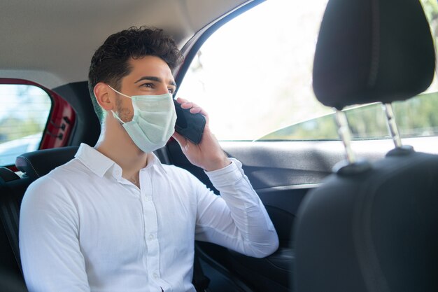 Retrato de hombre de negocios con mascarilla y hablando por teléfono de camino al trabajo en un coche. Concepto de negocio. Nuevo concepto de estilo de vida normal.