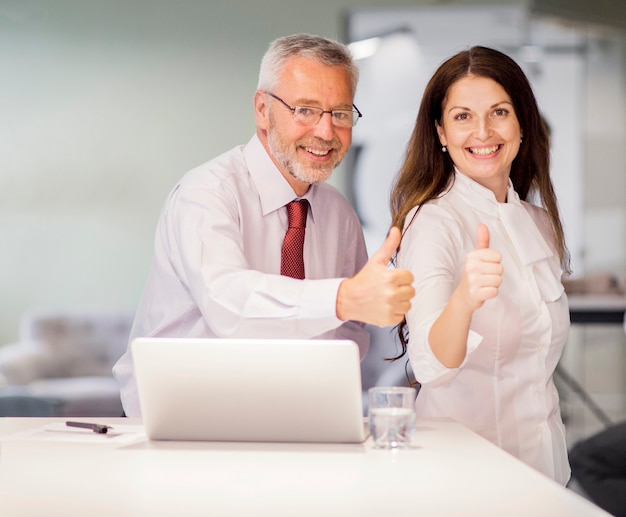 Foto gratuita el retrato del hombre de negocios mayor sonriente y la empresaria que muestran el pulgar para arriba firman adentro la oficina