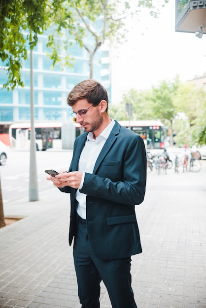 Retrato de un hombre de negocios de pie en la calle utilizando el teléfono móvil
