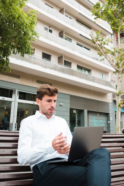 Retrato de un hombre de negocios que mira seriamente la computadora portátil delante del edificio