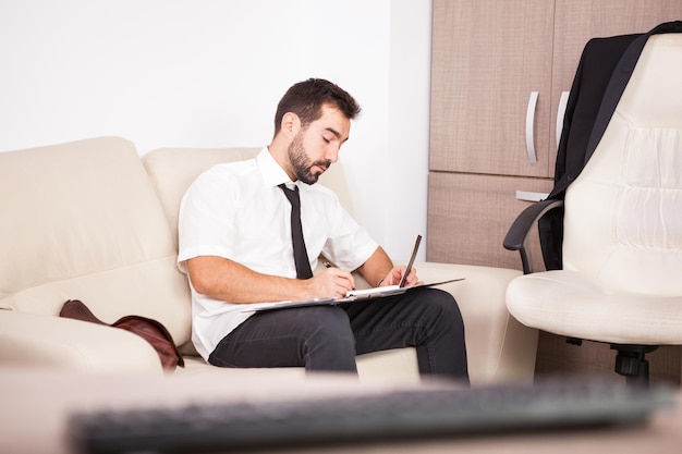 Retrato de hombre de negocios que trabaja en la oficina en el sofá poniendo largas horas de trabajo. Empresario en entorno profesional