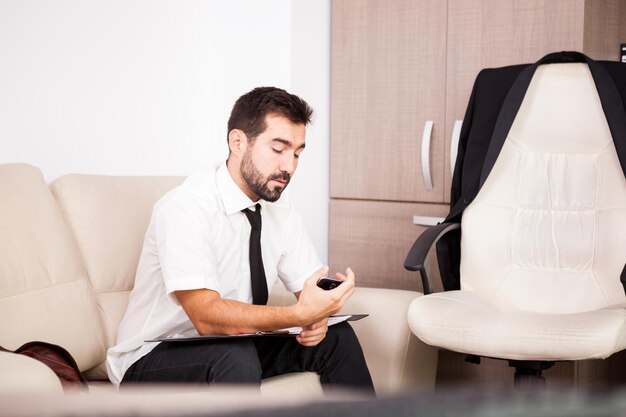 Retrato de hombre de negocios que trabaja en la oficina en el sofá poniendo largas horas de trabajo. Empresario en entorno profesional