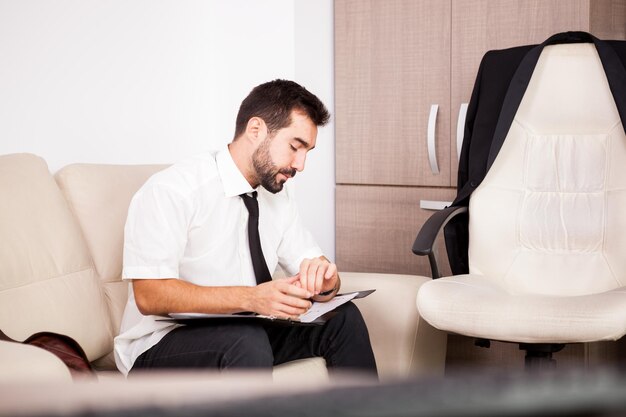 Retrato de hombre de negocios que trabaja en la oficina en el sofá poniendo largas horas de trabajo. Empresario en entorno profesional