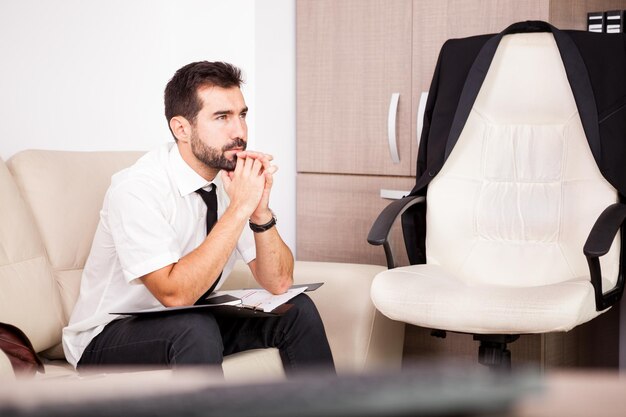 Retrato de hombre de negocios que trabaja en la oficina en el sofá poniendo largas horas de trabajo. Empresario en entorno profesional