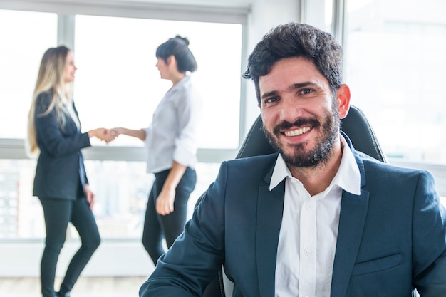 Retrato del hombre de negocios sonriente delante de las mujeres que sacuden las manos