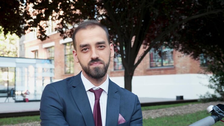 Foto gratuito retrato de hombre de negocios sonriente en traje diplomático mirando a la cámara de pie afuera frente a la oficina de la empresa de inicio. hombre emprendedor trabajando en presentación de marketing. concepto al aire libre