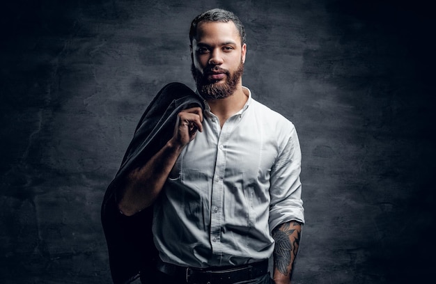 Retrato de un hombre negro barbudo con un brazo tatuado y una camisa blanca.