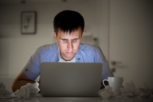 Retrato de un hombre con un ordenador portátil, tarde en la noche, la luz de la pantalla