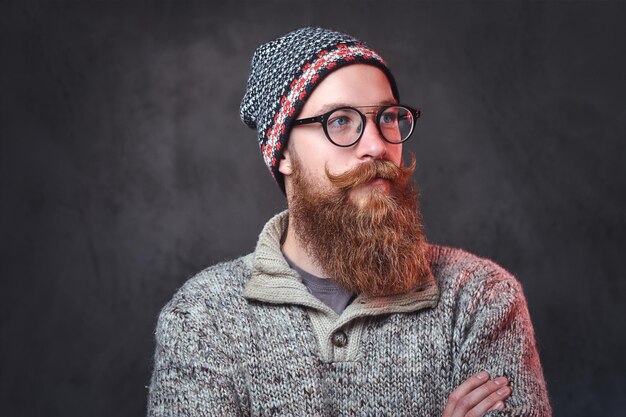 Retrato de un hombre pelirrojo barbudo con anteojos vestido con un suéter de lana y un sombrero.