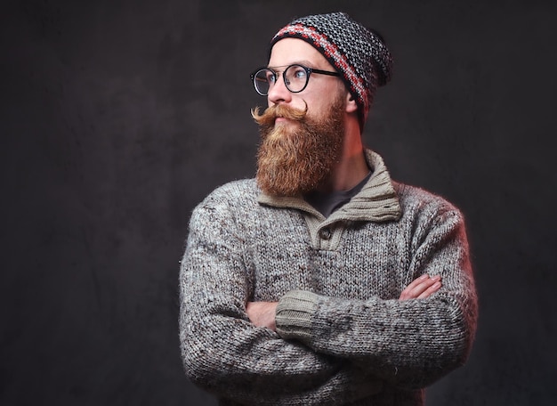 Retrato de un hombre pelirrojo barbudo con anteojos vestido con un suéter de lana y un sombrero.