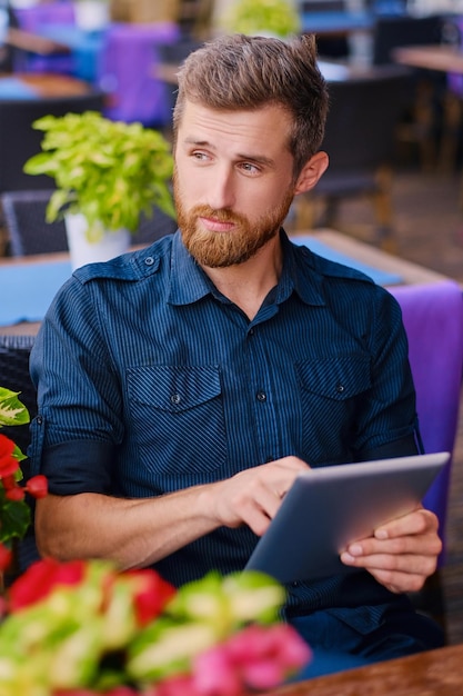 Foto gratuita retrato de hombre pelirrojo barbudo usando una tableta en la mesa.