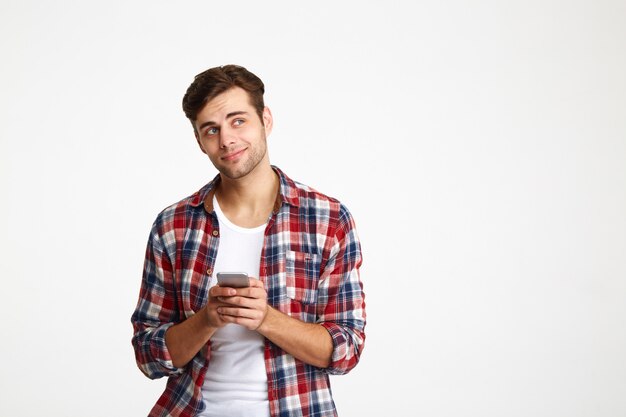 Retrato de un hombre pensativo sonriente que sostiene el teléfono móvil