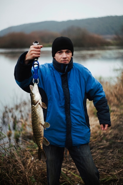 Foto gratuita retrato de hombre pesando pescado capturado cerca del lago