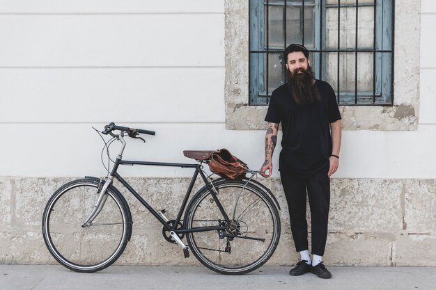 Retrato de un hombre de pie con la bicicleta apoyada en la pared