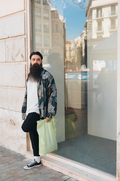 Retrato de un hombre de pie fuera de la tienda con bolsa de plástico en la mano