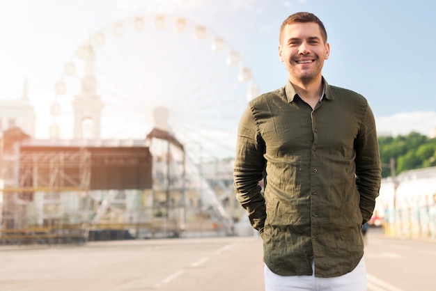 Retrato del hombre que se coloca cerca de la rueda de ferris en el parque de atracciones