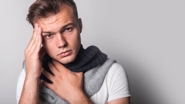 Retrato del hombre que tiene dolor de cabeza contra fondo gris