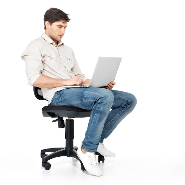 Retrato de un hombre que trabaja en la computadora portátil sentado en la silla - aislado en blanco.