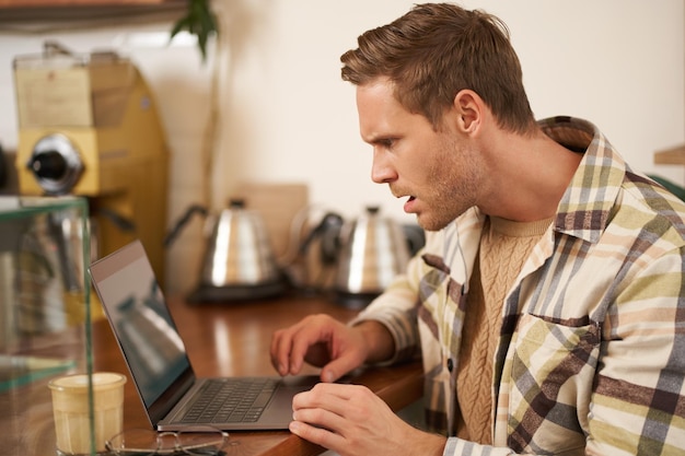 Foto gratuita retrato de un hombre que se ve frustrado en la pantalla de una computadora portátil mirando fijamente el monitor con una expresión facial conmocionada