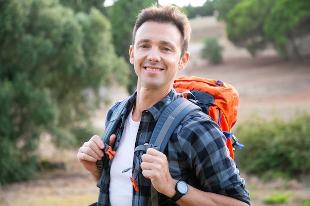 Retrato de hombre de raza caucásica de pie, sonriendo. Caminante feliz disfrutando de la naturaleza, llevando mochilas y posando. Concepto de turismo, aventura y vacaciones de verano.