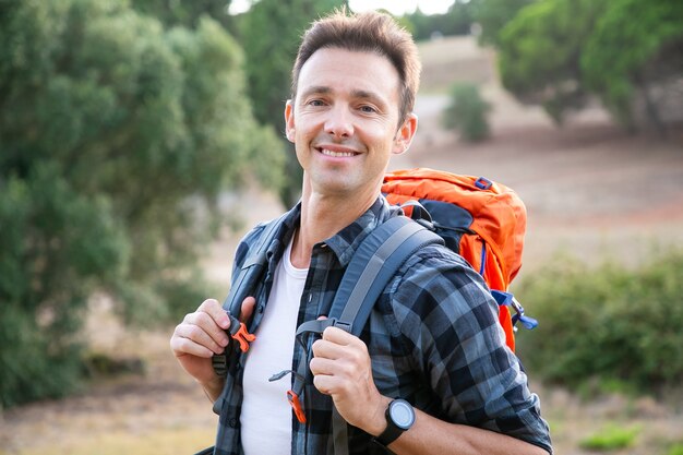 Retrato de hombre de raza caucásica de pie, sonriendo. Caminante feliz disfrutando de la naturaleza, llevando mochilas y posando. Concepto de turismo, aventura y vacaciones de verano.
