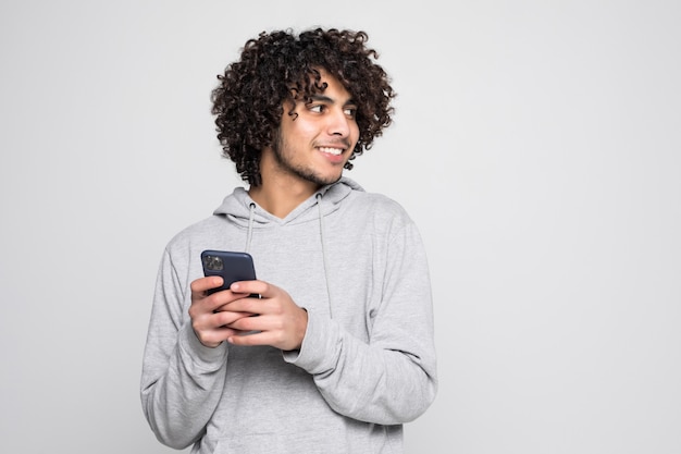 Retrato del hombre rizado hermoso que sostiene el teléfono aislado en la pared blanca