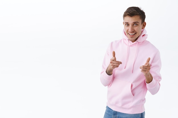 Retrato de hombre rubio guapo en sudadera con capucha rosa, que le invita a unirse al club