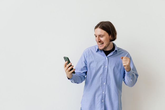 Retrato de hombre satisfecho feliz mirando el teléfono móvil y gritando aislado sobre fondo blanco.