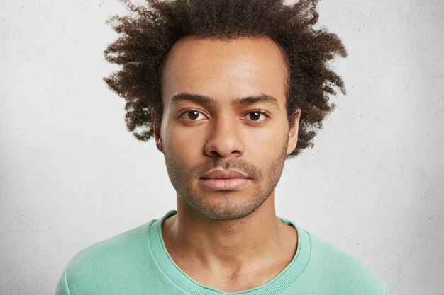Retrato de hombre seguro de piel oscura con peinado afro rizado tiene expresión facial tranquila,