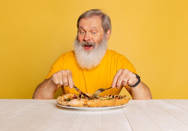 Retrato de hombre senior comiendo delicioso italiano aislado sobre fondo amarillo studio