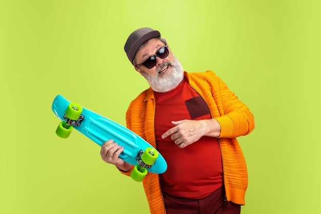 Foto gratuita retrato de hombre senior hipster sosteniendo un patín aislado sobre fondo verde.