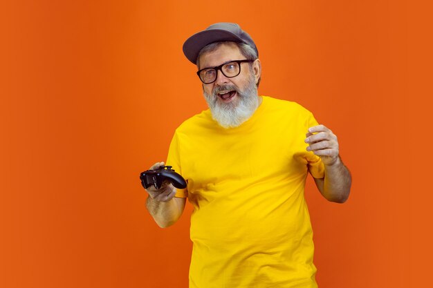 Retrato de hombre senior hipster usando dispositivos, gadgets aislados sobre fondo naranja studio. Tecnología y concepto de estilo de vida de ancianos alegre. T