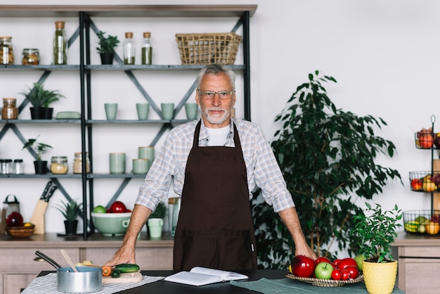 Foto gratuita retrato de hombre senior de pie detrás de la mesa en la cocina