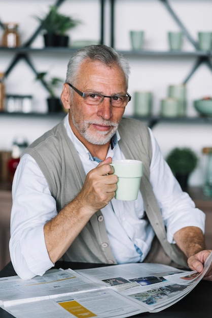 Retrato de hombre senior con taza de café en su mano leyendo periódico