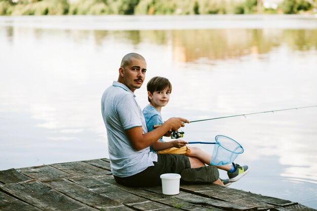 Retrato de un hombre sentado en el muelle con su hijo pescando en el lago