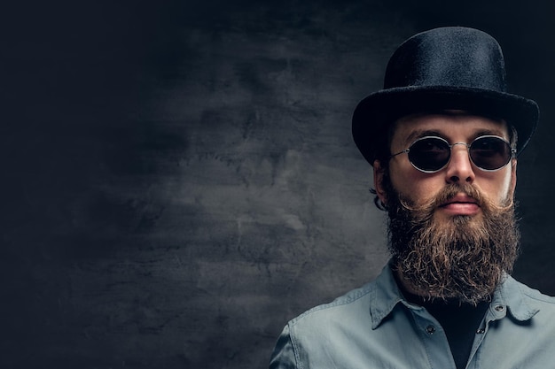 Retrato de un hombre serio y barbudo con gafas de sol y sombrero cilíndrico.