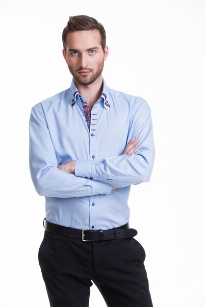 Retrato de hombre serio con camisa azul y pantalón negro con los brazos cruzados - aislado en blanco.