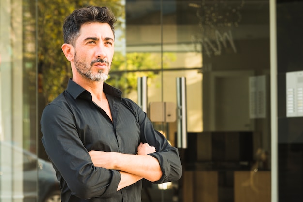 Retrato de hombre serio en camisa negra de pie frente a puerta cerrada