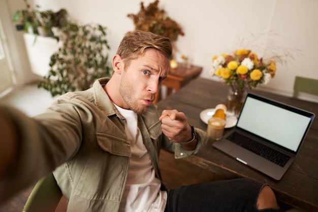 Foto gratuita retrato de un hombre serio que se toma una selfie con el puño y la cara amenazante se sienta en un café y posa en el café