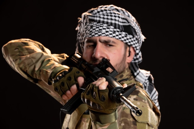 Retrato de hombre soldado en camuflaje luchando con ametralladora en una pared negra