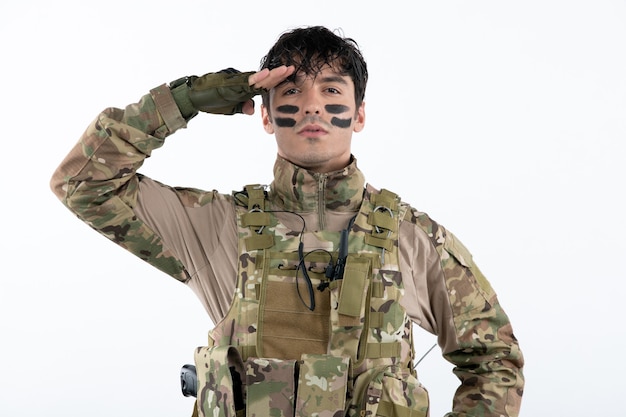 Retrato de hombre soldado en camuflaje saludando en la pared blanca