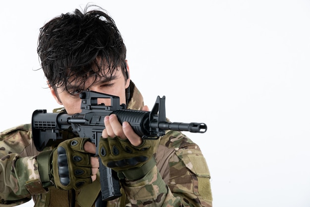 Retrato de hombre soldado en uniforme militar con rifle pared blanca