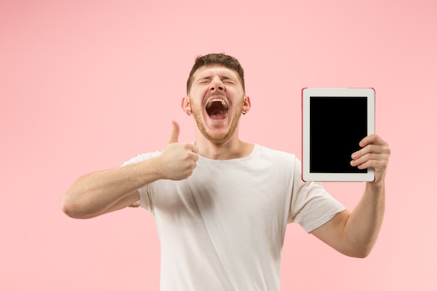 Retrato de hombre sonriente apuntando a la computadora portátil con pantalla en blanco aislada sobre fondo rosa studio. Las emociones humanas, el concepto de expresión facial y el concepto de publicidad.