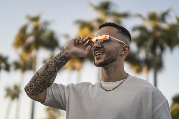 Retrato de un hombre sonriente con brazos tatuados y elegantes gafas de sol