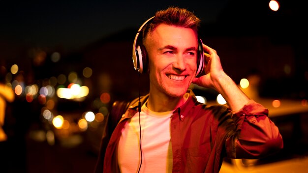 Retrato de hombre sonriente en la ciudad por la noche con auriculares