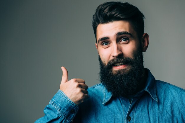 Retrato de un hombre sonriente con gafas mostrando el pulgar hacia arriba sobre la pared gris