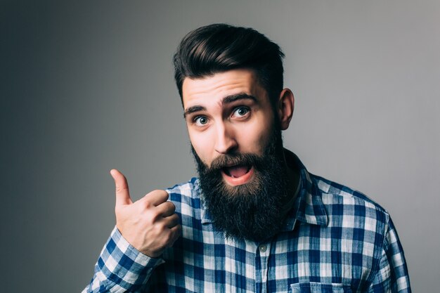 Retrato de un hombre sonriente con gafas mostrando el pulgar hacia arriba sobre la pared gris