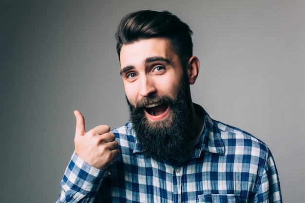 Retrato de un hombre sonriente con gafas mostrando el pulgar hacia arriba sobre la pared gris