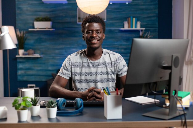 Retrato de un hombre sonriente mirando a la cámara mientras trabaja a distancia desde casa en un proyecto de negocios escribiendo un curso financiero en la computadora. hombre de negocios, sentado, en, escritorio, mesa, en, sala, oficina